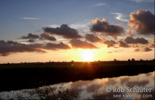 Wolkjes trekken voorbij terwijl de zon onder gaat met het silhouet van Haarlem op de achtergrond.