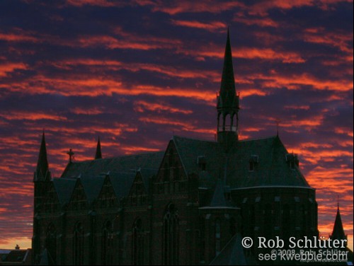 Rode wolken van een zonsondergang vormen een dreigende lucht boven een donkere kerk.