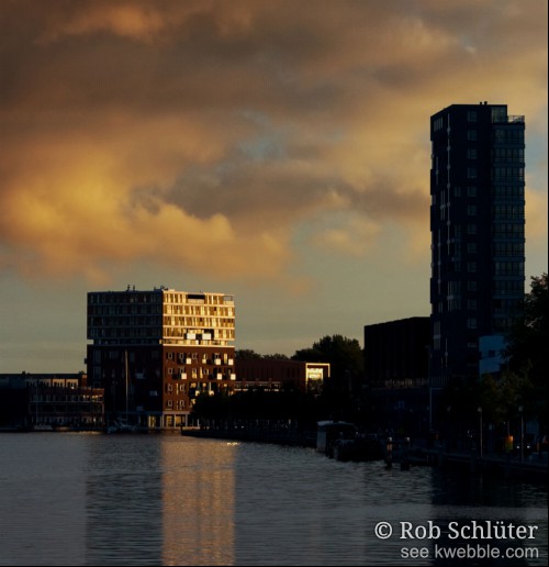 Gebouwen aan het Spaarne in Haarlem steken af tegen de door de zon oranje gekleurde wolkenlucht.