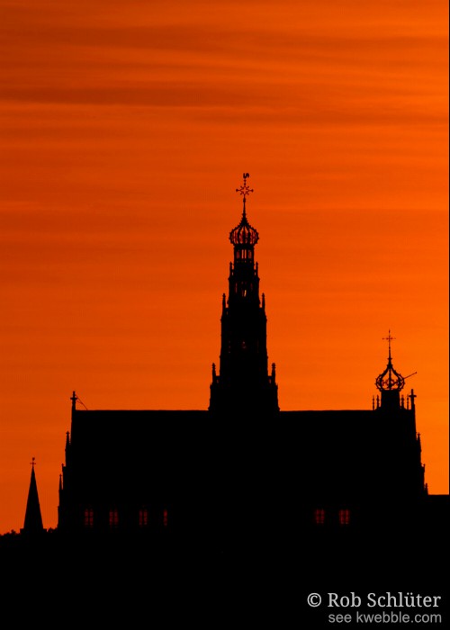 Tegen een donkeroranje lucht steken het silhouet van de Haarlemse Sint-Bavokerk en de toren van de Bakenesserkerk zwart af met de contouren van de ornamenten op de kerktorens, kroon, kruisen en haan duidelijk zichtbaar.