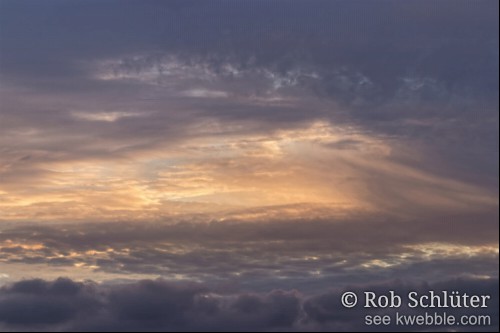 De ondergaande zon verlicht tussen grijze wolkenbogen door het midden tot de vorm van een oog.